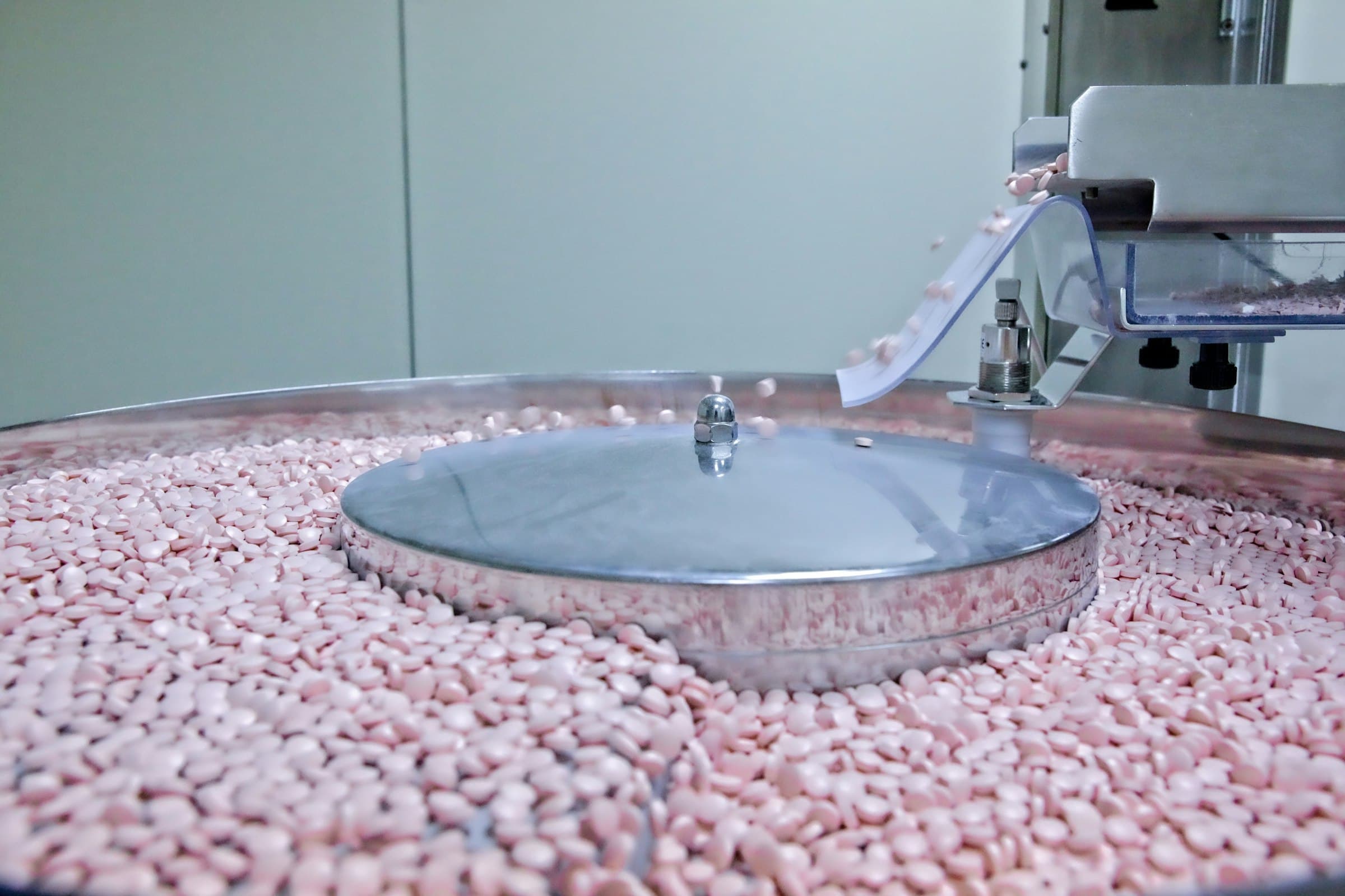 Pink tablets pouring from a tablet press into a collecting drum in a pharmaceutical plant